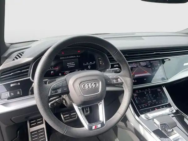 Das Bild zeigt das Inneninterieur eines AUDI Q8, aufgenommen aus der Sicht des Fahrers. Es zeigt das Lenkrad und das Armaturenbrett, welches schwarz ist.