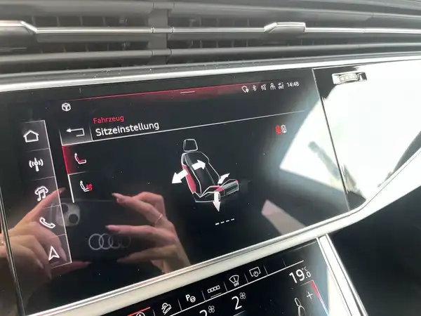 Dieses Bild zeigt das Innere eines AUDI Q8 mit einem Bildschirm, der die Sitz- und Fahrzeugeinstellungen anzeigt. Der Innenraum ist dunkel mit roten Akzenten.