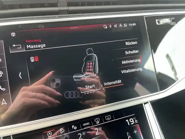 Das Bild zeigt den Innenraum eines Audi Q8 mit dem Display für die Massagefunktion der Sitze. Die Displayoberfläche ist schwarz mit verschiedenen Funktionen für Rücken und Schulter. Handschuhfach und andere Bedienelemente sind ebenfalls sichtbar.