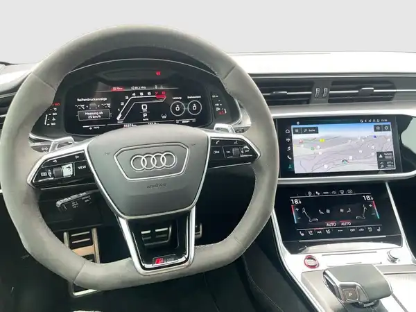 Das Bild zeigt das Innere eines AUDI QUAATTRO. Der Fokus liegt auf dem Lenkrad und dem Infotainment-Display, die predominantly schwarz sind. Es sind zudem markante Texteinblendungen auf dem Display vorhanden.