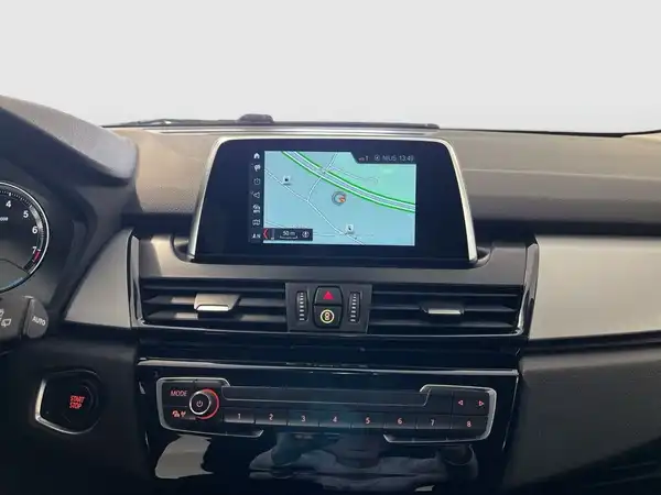 Das Bild zeigt das Innere eines BMW 225 mit einem schwarzen Interieur und einem Navigationsdisplay, das eine Karte anzeigt.