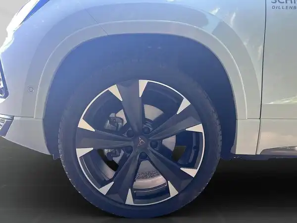 Das Bild zeigt das Rad eines weißen CUPRA ATECA aus der Seitenansicht, mit einem Händlerlogo im Hintergrund.