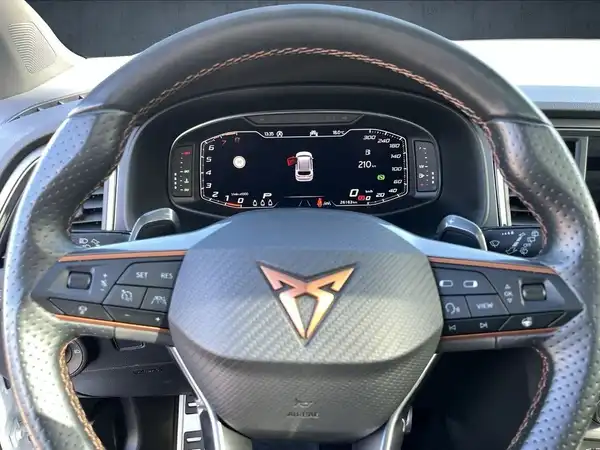 Das Bild zeigt das Innere eines CUPRA ATECA, mit einem Fokus auf das Lenkrad und das Armaturenbrett. Die Innenausstattung ist schwarz.