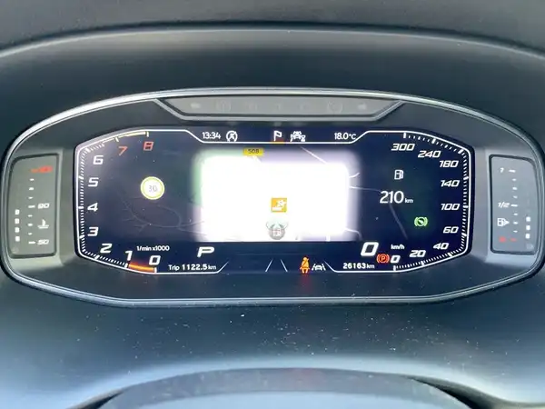 Das Bild zeigt das digitale Cockpit eines Fahrzeugs, das aus der Innenansicht aufgenommen wurde. Es hat ein schwarzes Interieur und enthält markante Texteinblendungen.