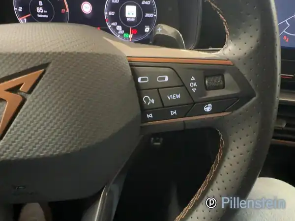 Das Bild zeigt das Interieur eines CUPRA FORMENTOR, insbesondere das Lenkrad mit Bedienelementen. Die Innenfarbe ist schwarz mit braunen Akzenten. Es enthält das Händlerlogo.