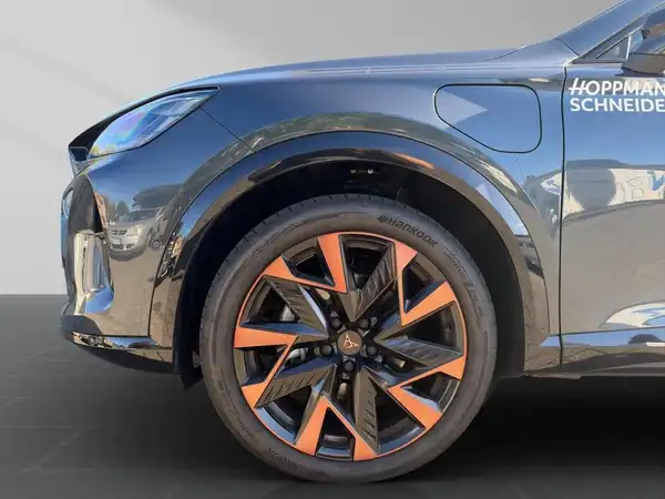 Das Bild zeigt einen CUPRA FORMENTOR von der Seite mit einem auffälligen Rad und orangefarbenen Akzenten. Im Hintergrund ist ein Händlerlogo sichtbar.