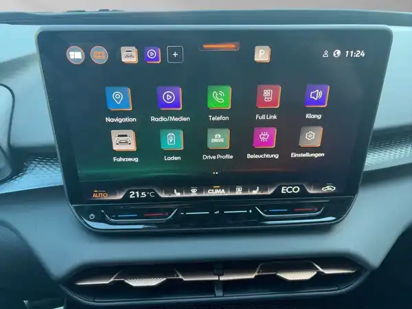 Aufnahme des Fahrzeuginnenraums mit einem Bildschirm, der verschiedene Funktionen anzeigt, darunter Navigation und Medien.