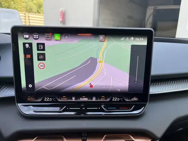 Das Bild zeigt das Innere eines Fahrzeugs mit dem Fokus auf einem Navigationsgerät, das eine Straßenkarte anzeigt. Es sind markante Texteinblendungen auf dem Bildschirm sichtbar.