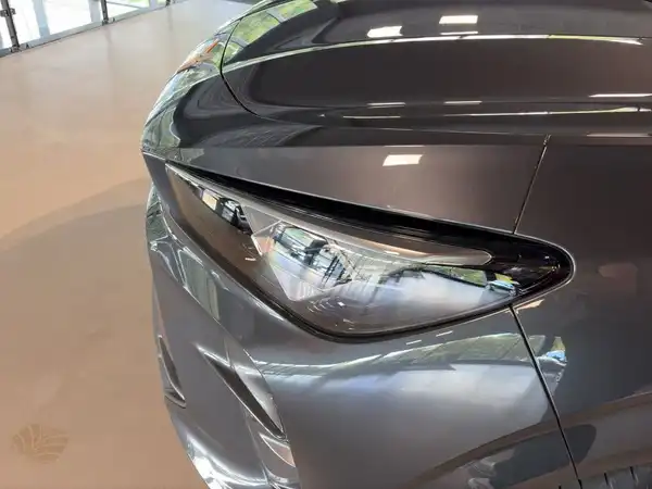 Das Bild zeigt den vorderen Bereich eines grauen Fahrzeugs, fokussiert auf den Scheinwerfer und einen Teil der Motorhaube.