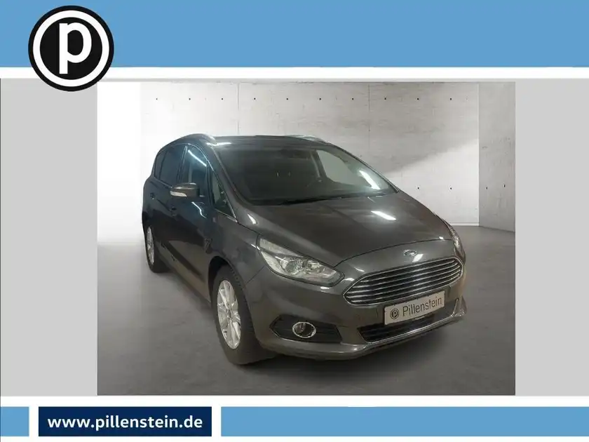 Das Bild zeigt einen grauen Ford S-MAX von vorne. Es enthält ein Händlerlogo und markante Texteinblendungen.