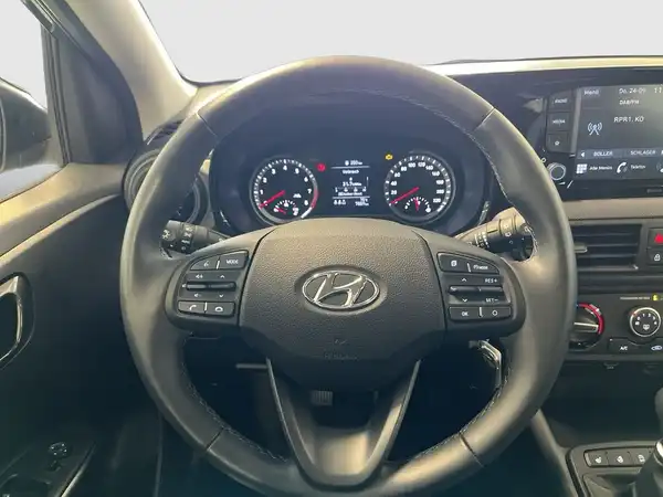 Das Bild zeigt das Innenraum eines Hyundai i10 mit einem schwarzen Interieur und dem Lenkrad im Fokus.