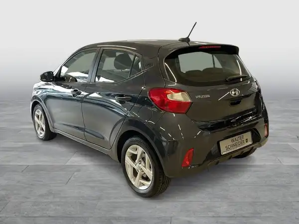 Das Bild zeigt einen schwarzen Hyundai i10 von hinten. Es ist ein Händlerlogo sichtbar, und es gibt markante Texteinblendungen.