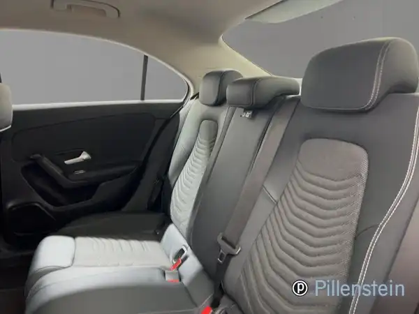 Das Bild zeigt den Innenraum eines Mercedes-Benz A 180 d, aufgenommen von hinten, mit einer schwarzen und grauen Innenausstattung. Das Händlerlogo 'Pillenstein' ist vorhanden.