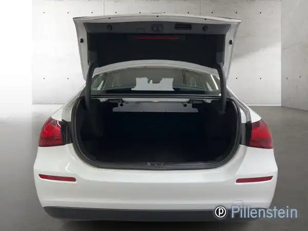 Das Bild zeigt den Kofferraum eines weißen Mercedes-Benz A 180 d, aufgenommen von hinten. Es ist ein Händlerlogo sichtbar.