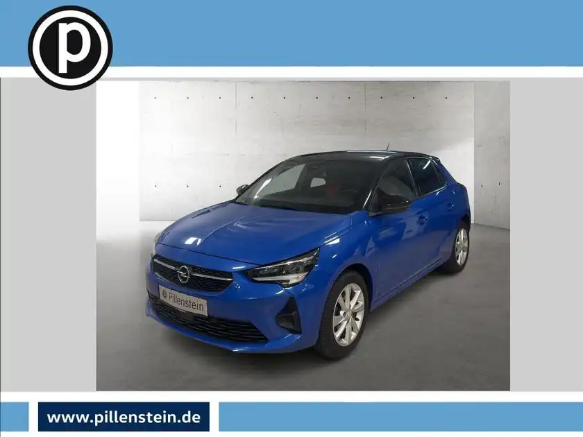 Das Bild zeigt einen blauen Opel Corsa aus der Frontalansicht. Es enthält das Händlerlogo und markante Texteinblendungen.