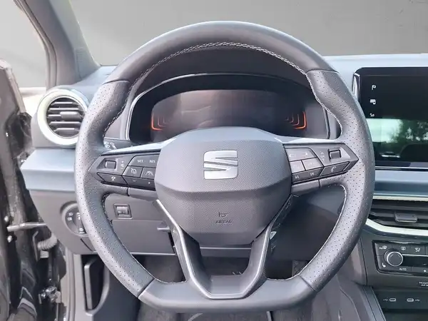 Das Bild zeigt das Innere eines SEAT Arona, mit einem Blick auf das Lenkrad und Armaturenbrett in schwarzer Farbe.