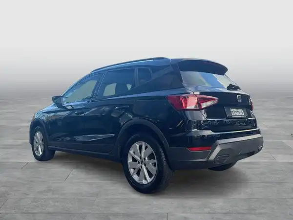 Das Foto zeigt die linke Seite eines schwarzen SEAT Arona. Es handelt sich um eine Aufnahme des Fahrzeugs von der Seite und es ist ein Händlerlogo auf dem Bild sichtbar.