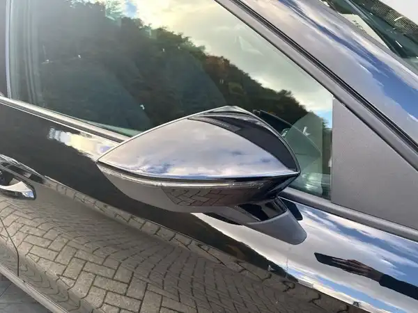 Das Bild zeigt den Seitenspiegel eines schwarzen SEAT Arona, aufgenommen aus einem seitlichen Blickwinkel.