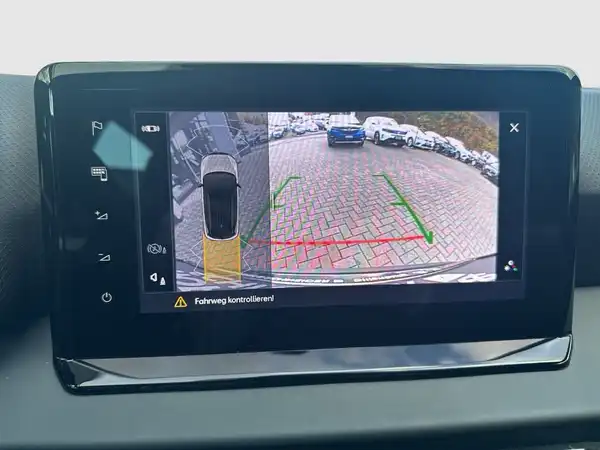 Eine Innenaufnahme des Fahrzeugs, die das Display eines Rückfahrkamerasystems zeigt. Die Anzeige enthält markante Texteinblendungen, die auf die Kontrolle des Fahrweges hinweisen.