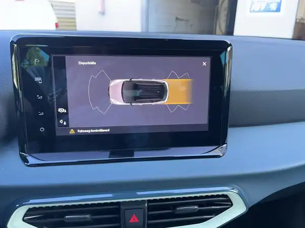 Das Bild zeigt den Innenraum eines SEAT Arona, speziell den Bildschirm mit einer Darstellung des Fahrzeugs sowie akustischen Warnhinweisen. Die Interieurfarbe ist schwarz.