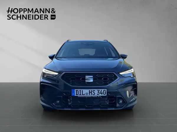 Das Bild zeigt einen blauen SEAT ARONA von vorne, mit einem Händlerlogo von HOPPMANN & SCHNEIDER.