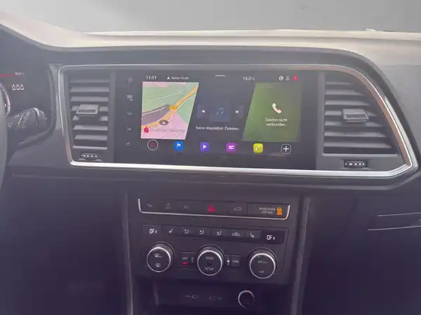 Das Bild zeigt das Innere eines Fahrzeugs, wobei ein Navigationsdisplay mit einer Karte und weiteren Funktionen sichtbar ist. Das Interieur ist schwarz.