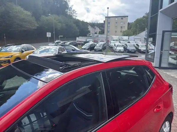 Die Aufnahme zeigt einen roten SEAT IBIZA von der Seite in einer Fahrzeugausstellung mit mehreren Autos im Hintergrund.