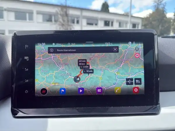 Das Bild zeigt das Navigationsgerät im Fahrzeug, das eine Karte mit Wegbeschreibung anzeigt. Es handelt sich um eine Innenaufnahme des Fahrzeugs.