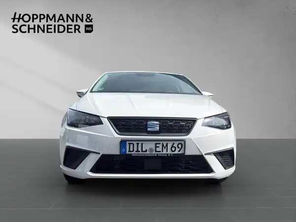 Das Bild zeigt einen weißen SEAT IBIZA von vorne. Es ist ein klarer und gut beleuchteter Aufnahme, mit dem Händlerlogo oben links.