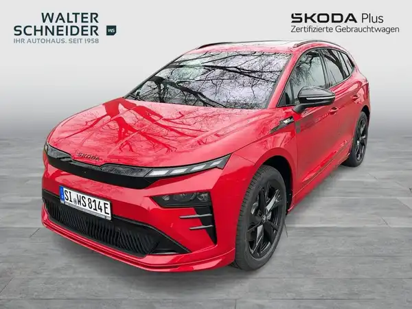 Das Bild zeigt einen roten ŠKODA ENYAQ iV von vorne. Im Hintergrund ist das Händlerlogo und weitere Texte zu sehen.