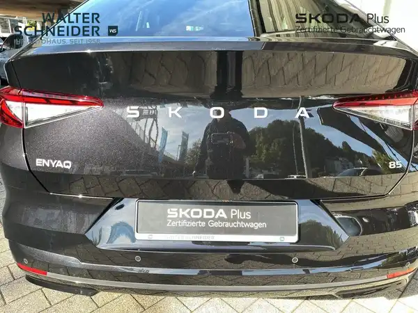 Das Bild zeigt die Rückansicht eines schwarzen ŠKODA ENYAQ iV. Im Hintergrund sind das Händlerlogo und weitere Textelemente sichtbar.