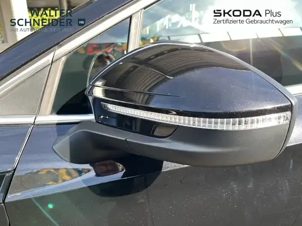 Seitenansicht des Fahrzeugs, ein schwarzer ŠKODA ENYAQ iV, mit Logos des Händlers. Es sind markante Texteinblendungen sichtbar.