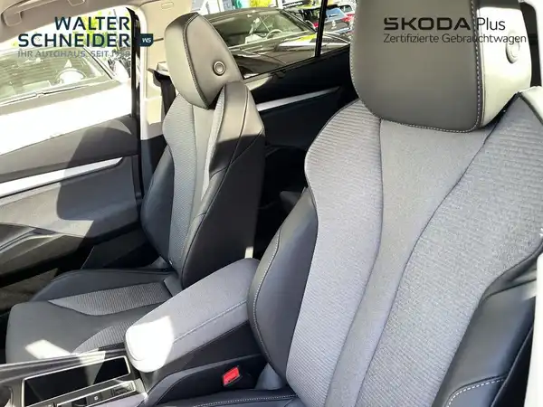Das Bild zeigt den Innenraum eines ŠKODA ENYAQ iV mit schwarzen und grauen Sitzen. Es sind Händlerlogos sichtbar.
