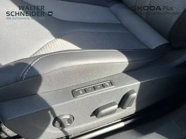 Nahaufnahme des Fahrzeuginnenraums des ŠKODA ENYAQ iV, mit einem grauen und beigen Interieur. Das Bild zeigt die Bedienelemente der Fahrzeugsitzverstellung. Händlerinformationen sind eingeblendet.
