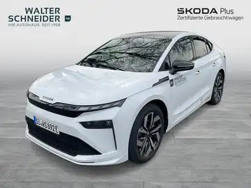 Das Bild zeigt einen weißen ŠKODA ENYAQ iV von der Seite. Im Hintergrund sind Händlerlogos und markante Texteinblendungen zu sehen.