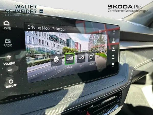 Das Bild zeigt das Innere eines ŠKODA Fahrzeugs mit einer Anzeige für die Auswahl des Fahrmodus. Der Innenraum ist schwarz und es ist ein Händlerinformation eingeblendet.