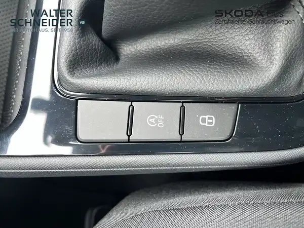 Das Bild zeigt die Innenansicht eines Schaltbereichs mit Knöpfen in einem ŠKODA Fahrzeug. Die dominant Farbe des Innenraums ist schwarz. Es sind Händlerlogos und markante Texteinblendungen zu sehen.