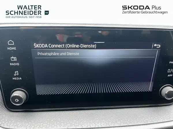Innenaufnahme des ŠKODA Fahrzeugs, Bildschirm zeigt Online-Dienste an. Händlerlogo ist eingeblendet, es sind markante Texteinblendungen vorhanden.