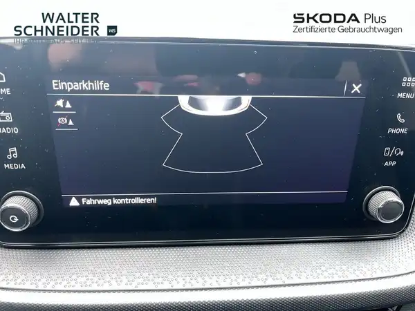 Die Innenaufnahme zeigt das Infotainment-System eines ŠKODA, mit dem Display für die Einparkhilfe. Das Auto-Inneninterieur ist dunkel (schwarz) und das Händlerlogo ist sichtbar.