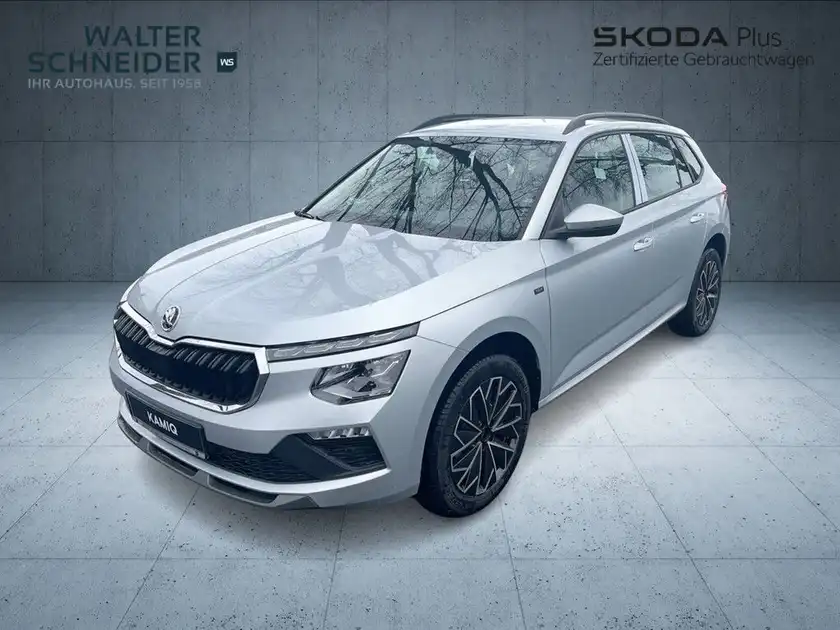 Das Bild zeigt einen ŠKODA KAMIQ von der Seite. Das Fahrzeug ist in der Farbe Weiß. Es ist ein Händlerlogo sichtbar.