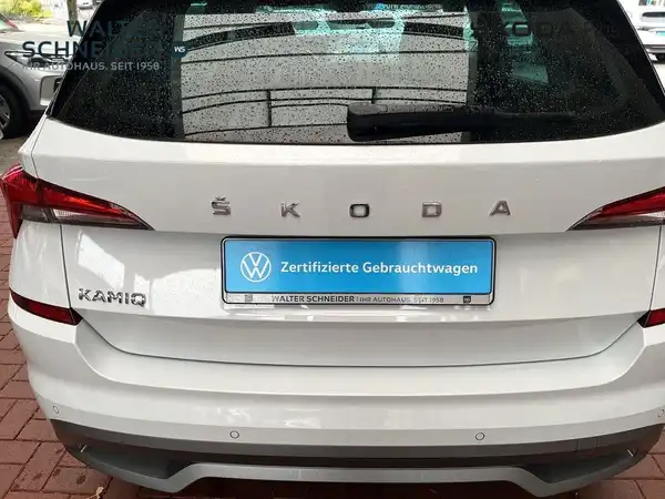 Das Bild zeigt einen weißen ŠKODA KAMIQ aus der Rückansicht, mit einem Händlerlogo und einer markanten Texteinblendung.