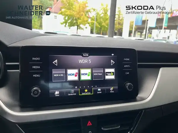 Eine Innenaufnahme des Fahrzeugs, die das Display und die Armaturen zeigt. Das Interieur ist schwarz und das Händlerlogo ist eingeblendet.