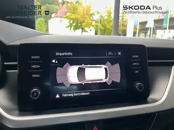 Eine Innenaufnahme des Fahrzeugs, die das Navigationsdisplay mit Einparkhilfe zeigt, in schwarzem Interieur. Das Händlerschild ist vorhanden und es gibt markante Texteinblendungen.