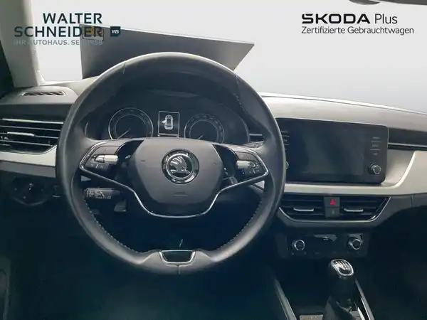 Das Bild zeigt das Innere eines ŠKODA KAMIQ. Es ist eine Innenaufnahme mit schwarzem Interieur und es sind Händlerlogos sowie markante Texteinblendungen vorhanden.