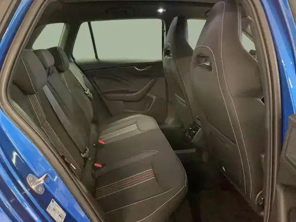 Das Bild zeigt das Innere eines blauen ŠKODA KAMIQ aus einer Innenaufnahme. Es zeigt die Rückbank, die mit schwarzem Stoff und roten Akzenten ausgestattet ist.