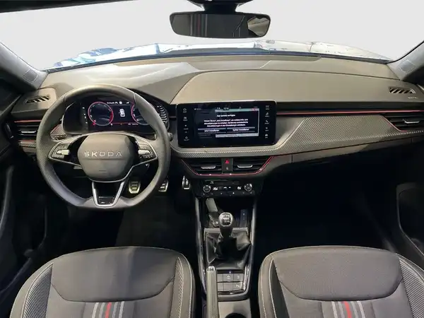 Innenaufnahme des ŠKODA KAMIQ mit schwarzem Interieur und roten Akzenten, zeigt das Armaturenbrett und das Infotainment-System.