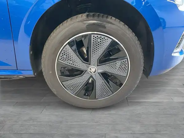 Das Bild zeigt die Seite eines blauen ŠKODA KAMIQ, das Rad mit einem modernen Felgendesign ist gut sichtbar.