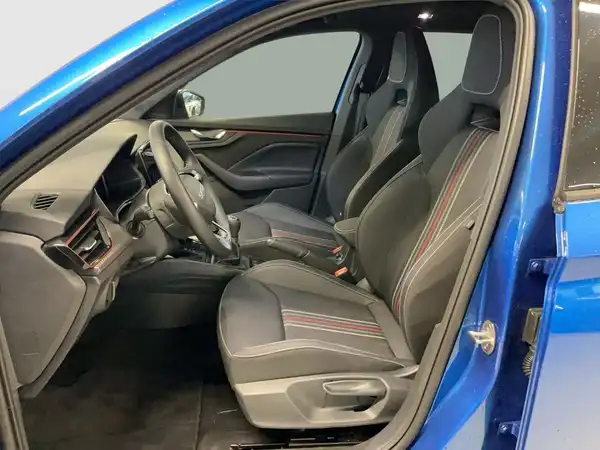 Das Bild zeigt das Innenraum eines blauen ŠKODA KAMIQ, aufgenommen von der Beifahrerseite. Die Sitze sind schwarz mit roten Akzenten.