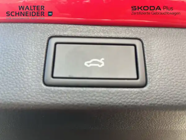 Innenaufnahme eines Fahrzeugs, die eine Taste zeigt. Das Interieur ist schwarz. Das Bild enthält ein Händlerlogo und Texteinblendungen.