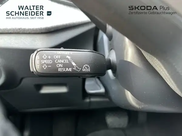 Das Bild zeigt eine Innenaufnahme des ŠKODA KAMIQ, spezifisch einen Teil des Armaturenbretts mit einer Bedieneinheit. Der Innenraum ist in schwarz gehalten. Auf dem Bild sind die Logos des Händlers zu sehen und es enthält markante Texteinblendungen.